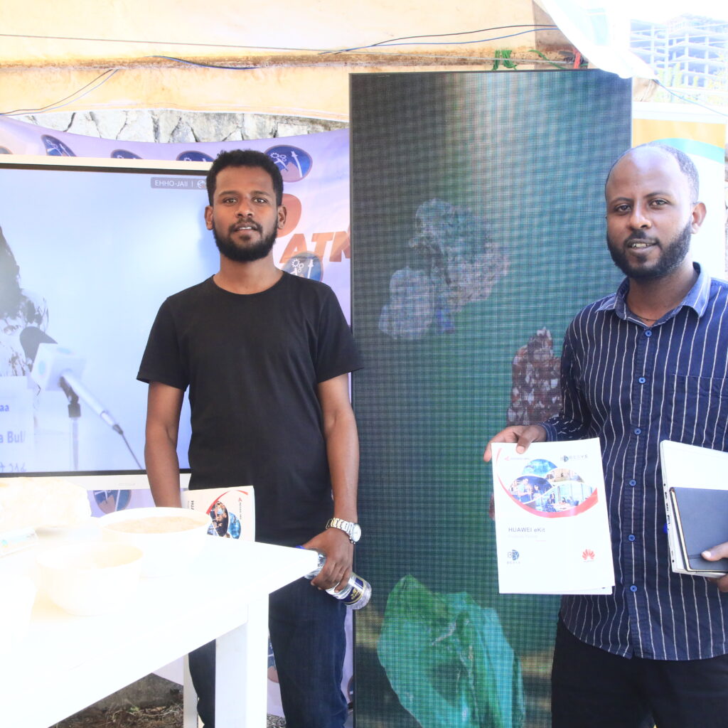 Two BESYS Technologies team members presenting a Huawei eKit catalog and technical solutions like Digital Signage at a professional exhibition booth featuring digital displays and industrial mineral samples.